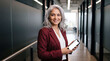 © The Stock Hub - Senior adult woman holding smartphone in modern office hallway smiling at camera business technology concept