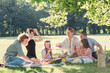 © Soloviova Liudmyla - Large happy group of family and friends enjoying relaxing outdoor summer picnic under big green tree in sunny peaceful park eating fresh food and sitting on cozy blanket laughing and talking together