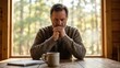 © Hala - Thoughtful man sitting alone at wooden table by cabin window deep in reflection