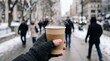 © Felippe Lopes - Person holding a steaming cup of coffee on a snowy city street in winter