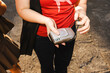 © Studio Marmellata - Close-up of a woman in a red t-shirt holding a silver vintage compact film camera in her hands outdoors on a paved street. She adjusts the black wrist strap.