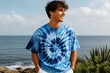 © mila103 - Young man smiling on coastline wearing tie dye shirt