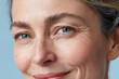 © JoeyMarut - Mature woman close up portrait showing mild skin dehydration lines under eyes and natural smile with pastel blue background conveying calm confidence
