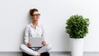 © 69 - Thoughtful young woman sitting on the floor in a casual white shirt and glasses holding a laptop, looking away thoughtfully near a large green indoor plant in white pot