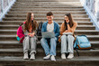 © InsideCreativeHouse - Group of high school students sitting on campus stairs with textbooks and laptop, classmates talking together, digital learning, education and student life concept