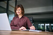 © Stock 4 You - Mid age businesswoman taking notes in notebook looking at laptop screen in office. Mature woman business consultant writing agenda with pen at desk. Female advisor prepares strategy plan at work.