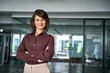 © Stock 4 You - Portrait of confident businesswoman in 40s standing with arms crossed in office at copy space. Mature woman boss looks at camera with light smile. Trustworthy female business chief leads company.