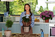 © Home-stock - Smiling woman in gardening apron and gloves displaying beautiful potted hydrangea surrounded by gardening tools and houseplants in kitchen interior