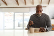 © Wavebreak Media - Senior African man sitting at home table wearing shirt holding ceramic bowl and spoon, copy space