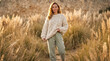 © MargoD - Smiling young woman wearing sustainable fashion clothes with cheerful and peaceful mood posing during outdoor walk against golden pampas grass and impressionistic textured background