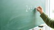 © SashaMagic - Child's hand writing 2+3=5 on a green chalkboard, close-up of learning math in an elementary classroom