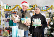 © JackF - Elderly couple chooses holiday kits of care products in a supermarket decorated for Christmas. Wife and husband in a Santa hat doing New Year's shopping in a household store