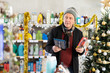 © JackF - Mature man pulls a razor and a hair trimmer in his hands and chooses which one to take. Man buying razors on the background of a Christmas tree in a supermarket