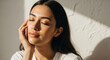 © Md - Serene young woman touching face softly with eyes closed bathed in morning sunlight highlighting natural beauty and glowing healthy skin texture.