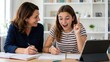© Tati - Adult woman tutoring a teenage girl at a tablet, both smiling and writing in notebooks during a home study session