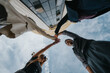 © qunica.com - A diverse business team stands outdoors and joins hands above their heads in a team gesture.