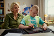 © DragonImages - Caucasian boy with Down Syndrome drawing on tactile learning board while middle aged Caucasian woman guiding at desk. Supporting inclusive education, useful for therapy or caregiving campaigns