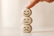 © crispy - Woman hand stacking stone icons with happy neutral and sad emoticon faces. Concept of choosing mood and mental health survey. Emotional state assessment and feedback tool for psychology