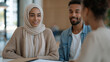 © forenna - Financial counselor seated across from a young couple in a community center office, folders open on the table, workplace financial wellness program, credit counseling, employee