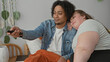 © Krakenimages.com - Woman rests head on man's shoulder while he holds a remote and orange blanket on a bed inside a building; cozy together affection.