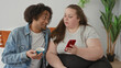 © Krakenimages.com - Woman holding red smartphone showing the screen to man who leans in while holding a blue coffee cup seated together on bed; quiet intimacy.