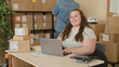 © Krakenimages.com - Woman typing on laptop and sorting shipping parcels at a packing desk with stacked boxes and labels in building; entrepreneurship confidence.