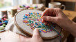 © Heba - Close up of person hands hand-stitching beautiful colorful floral design on linen fabric using wooden hoop with needle and thread in cozy workshop room