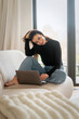 © gzorgz - Confident young woman sitting on a couch in her modern home and using a notebook for work