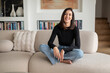 © gzorgz - Smiling brunette haired woman relaxing on a sofa in her modern home interior