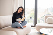 © gzorgz - Full length of a brunette haired young woman reading a book in her modern home