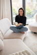 © gzorgz - Full length of a brunette haired young woman reading a book in her modern home