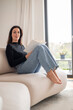 © gzorgz - Full length of a brunette haired young woman reading a book in her modern home