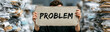 © pattozher - Surrounded by Piles of Paper: A person stands in front of towering stacks of discarded paper, holding a sign that reads PROBLEM, symbolizing overwhelm and a challenging situation.