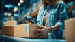 © Dao - Female seller worker online store holding scanner scanning parcel barcode tag packing ecommerce post shipping box checking online retail store orders in dropshipping delivery service warehouse.