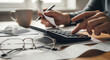 © fitria - Person calculating household expenses using a calculator and reviewing financial documents at a desk.