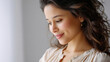 © Liliya - Portrait of a young woman with wavy hair smiling gently and looking down, natural light, soft background.