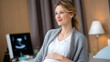 © Liliya - Happy pregnant woman sitting in a modern clinic, smiling and touching her belly, with ultrasound monitor in the background.