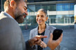 © Marko Geber - Smiling business colleagues reviewing smartphone outside office
