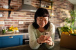 © Davor - Smiling woman using smartphone in cozy home kitchen