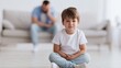 © Bonsales - Little boy sitting on floor crying, facing a challenging family situation with his father blurred in the background on a sofa