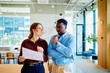 © we.bond.creations - Two diverse business people collaborating, analyzing document data, having a discussion in a modern office environment