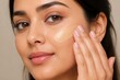 © Babb - A person uses their fingers to apply foundation to their face. The setting is bright with good lighting. The individual appears focused on their makeup process.