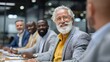 © Anuson - Smiling senior man with glasses and beard at a diverse business meeting, happy and confident while discussing with colleagues