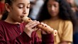 © Tima - Girl playing recorder instrument in music class. Young student learning to play woodwind flute during school lesson. Artistic education concept for creative child development programs.