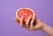 © Mustafa Kawa - Hand holding a fresh half of a grapefruit isolated on a purple background