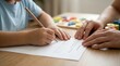 © MheeP - A child practicing handwriting with the help of an adult on a wooden desk.