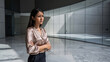 © Miftakhul - Worried businesswoman looking away in modern office lobby with marble floors and glass walls, concept for career stress, anxiety and workplace challenges