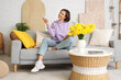 © Pixel-Shot - Smiling young woman with air conditioner remote control and magazine sitting on sofa in living room