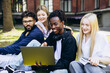 © Petro - Group of diverse college students studying and working together outdoors on a laptop, sharing ideas and smiling
