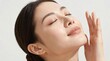 © FANGWORLD - A serene young Asian woman with glowing clear skin gently touches her cheek with closed eyes representing natural beauty skincare routine and wellness